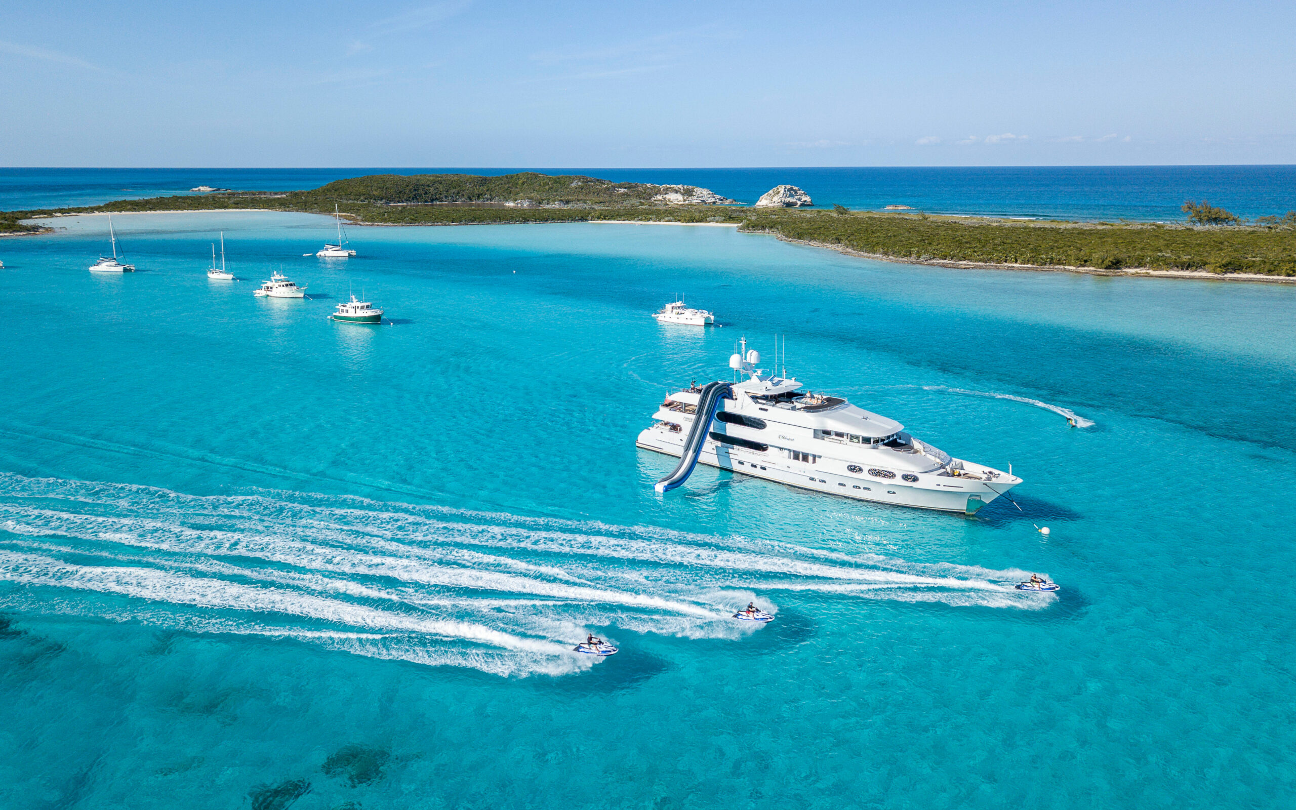 Motor yacht at anchor off a sandy cay in the Bahamas, guests out on jet skis