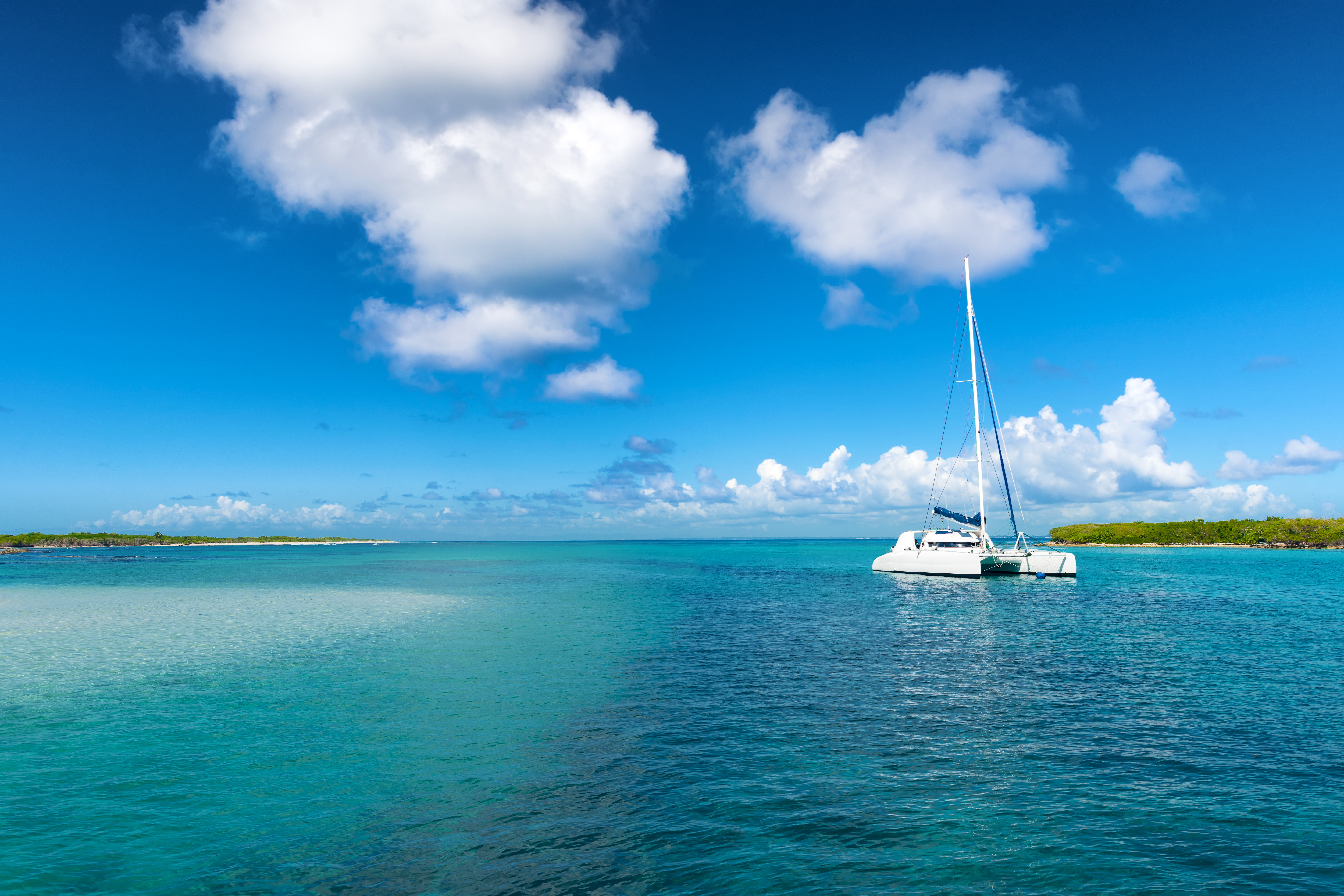 Crewed sailing catamaran at anchor in shallow turquoise water